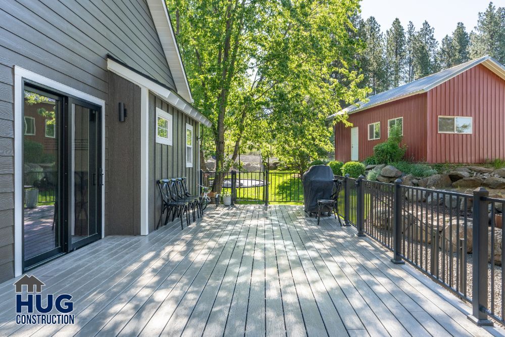 Spacious wooden deck with outdoor furniture and grill, overlooking a landscaped yard with trees, remodels and additions, and a red outbuilding.