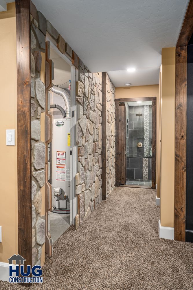Interior hallway with stone walls, carpeted floor, and recent remodels including a visible water heater on the left leading to a glass door.