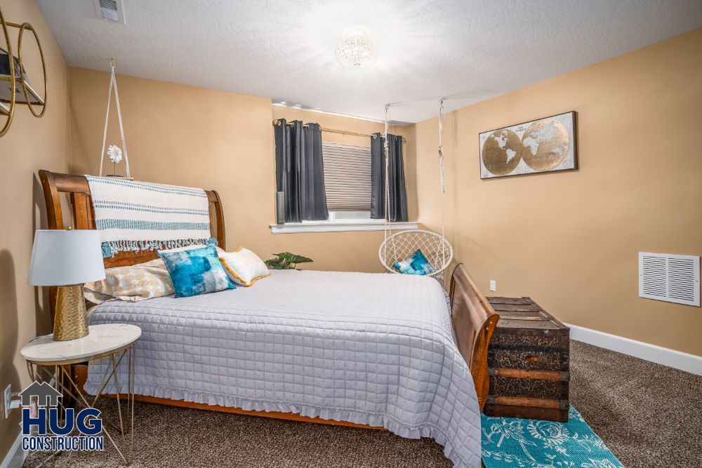 Cozy bedroom with a neatly made bed, complementary earth tone decor, and a small window with dark curtains after recent remodels and additions.