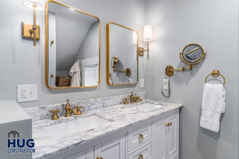 Modern bathroom interior with remodels and additions, featuring dual sinks, gold fixtures, and a marble countertop.
