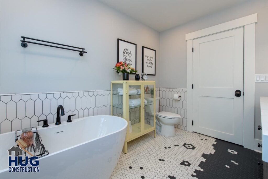 Elegant monochrome bathroom remodels with freestanding tub, hexagonal tile flooring, and decorative wall art.