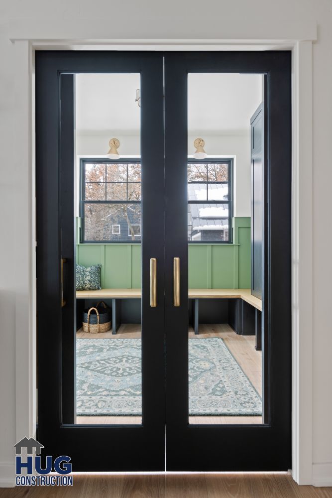 Double doors with glass panels opening into a remodeled room with green cabinetry and patterned rug.