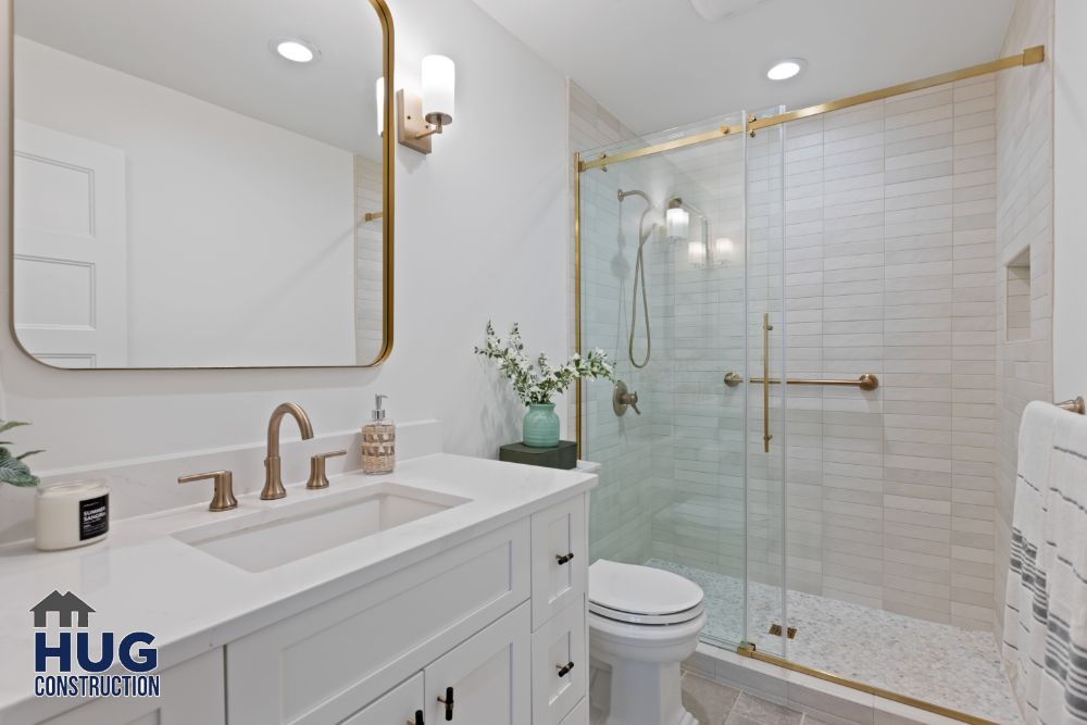 Remodeled modern bathroom with white vanity, brass fixtures, and glass-enclosed shower.