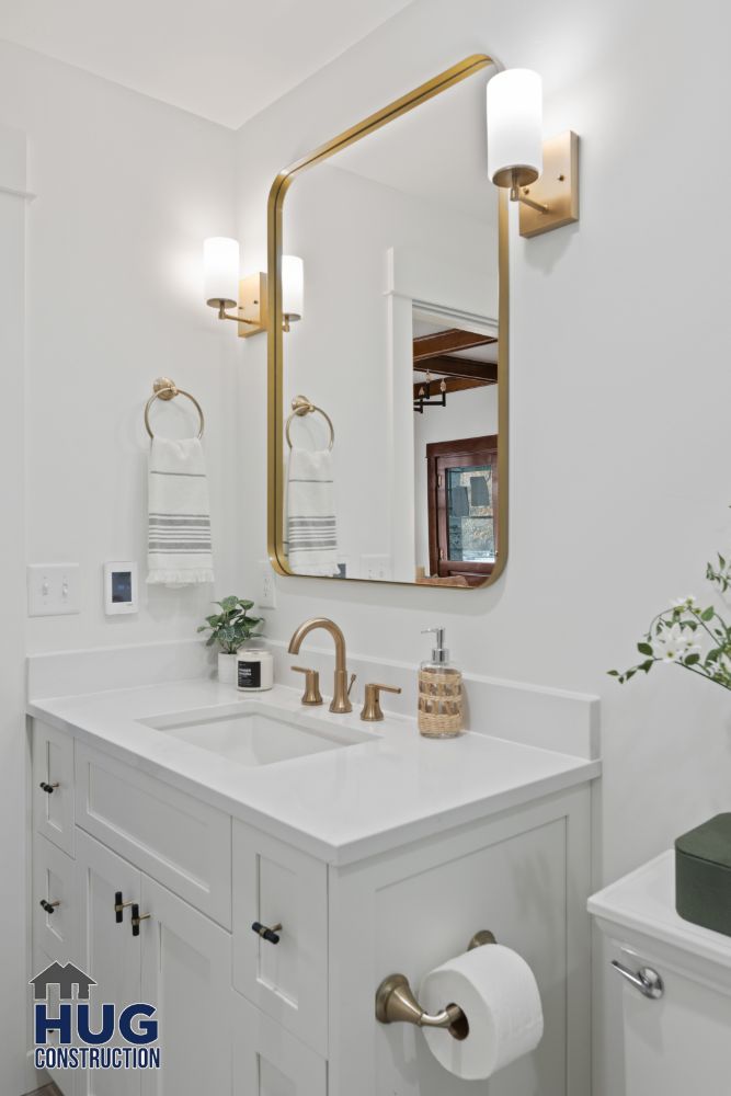 Modern bathroom interior with white vanity, brass fixtures, rectangular mirror, and recent remodels.