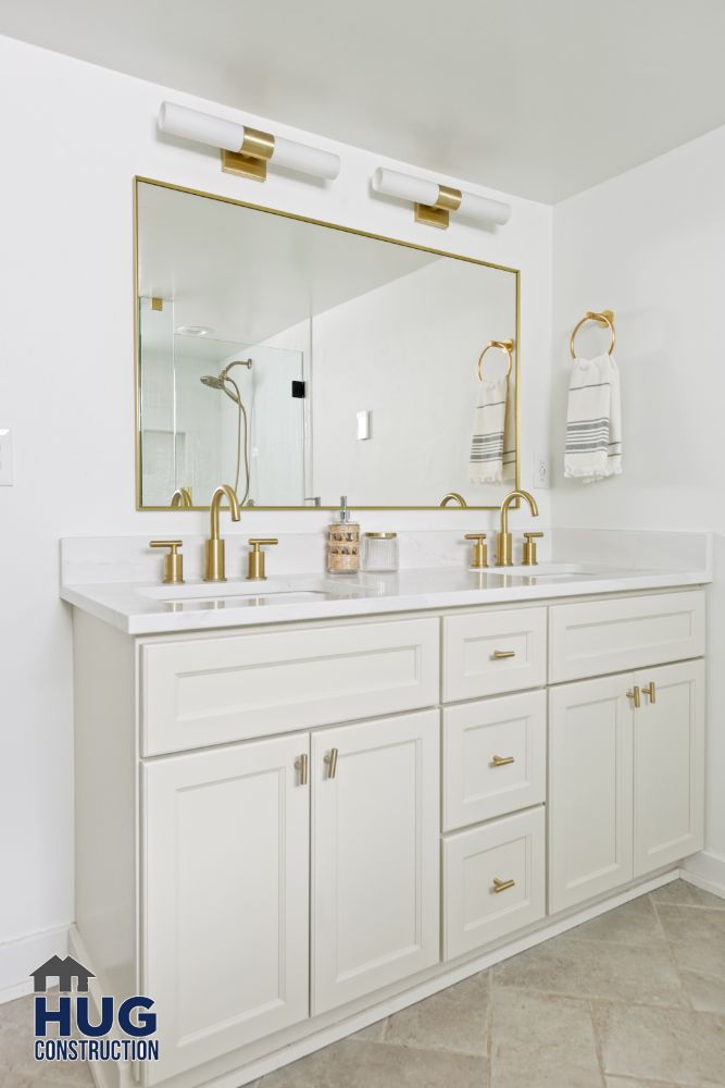 Modern bathroom remodels with gold fixtures and white cabinetry.