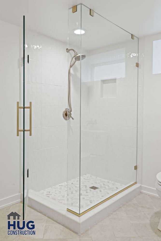 Modern glass-encased shower remodels with white tile and gold accents.