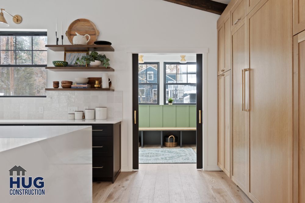 Modern kitchen interior with wooden cabinetry and open shelving, featuring additions like a view into an adjoining room with a green door.