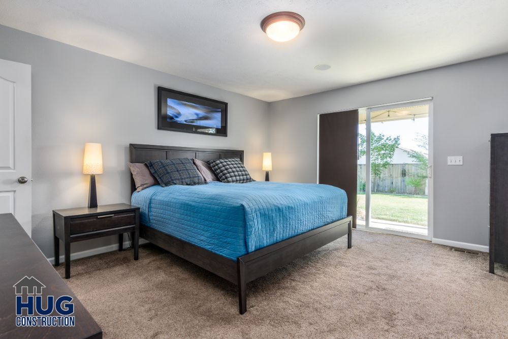 A neatly arranged bedroom with a blue bedspread, two table lamps, a sliding door leading to the backyard, and recent remodels.