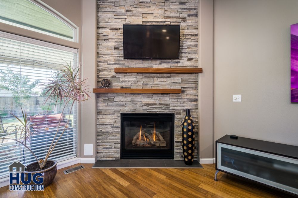 Modern living room with a stone fireplace, mounted television, and hardwood floors, featuring recent remodels.