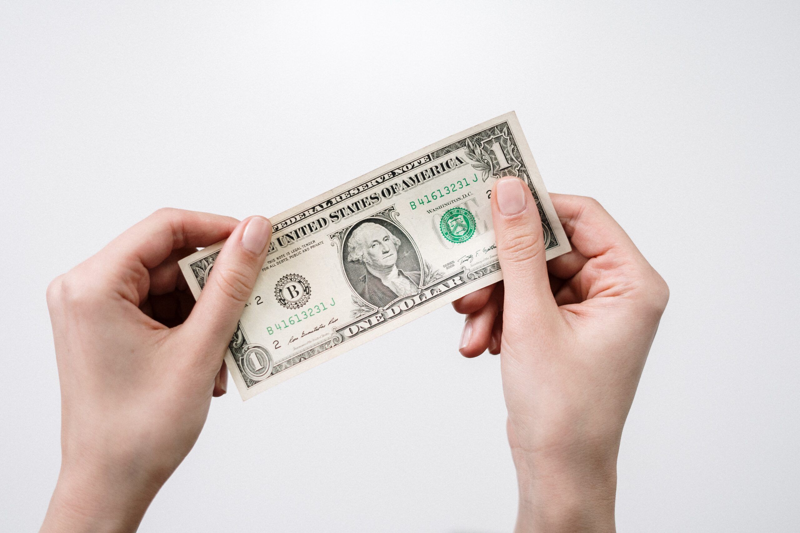 Two hands holding a one-dollar bill against a white background, illustrating pricing strategies.