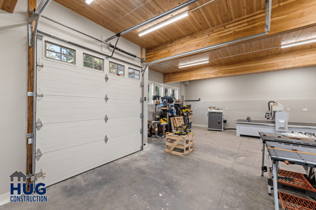 A spacious and tidy Radio Ln Garage & ADU with a wooden ceiling, featuring an array of tools and equipment neatly organized on shelves and a workbench, with a closed white garage door on one side