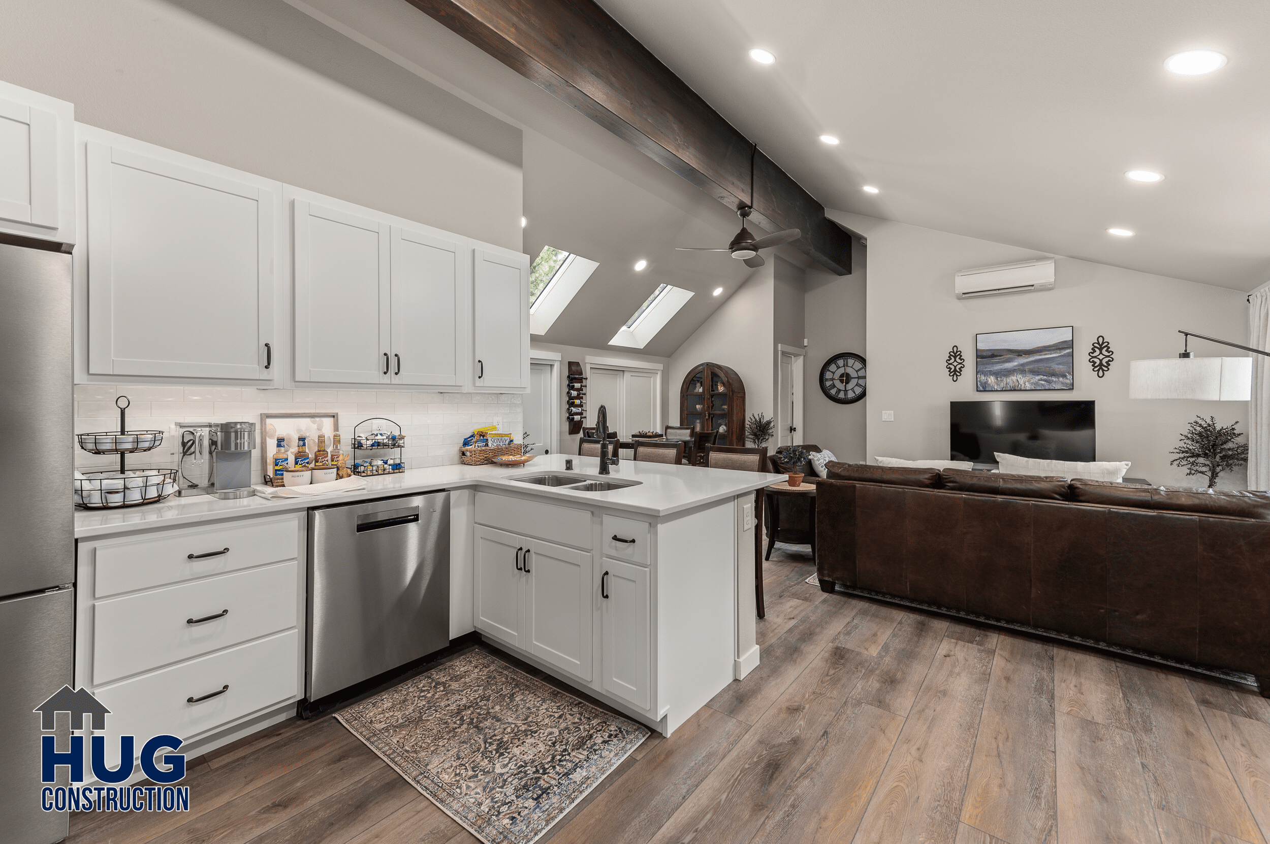 Modern kitchen with white cabinetry and stainless steel appliances, opening up to a cozy living area with a brown sofa and hardwood floors on Radio Ln.