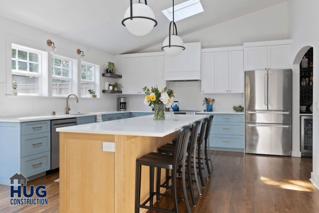A bright and spacious modern kitchen addition, with white cabinetry, stainless steel appliances, a wooden island with seating, and pendant lighting.