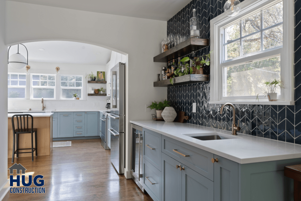 A modern kitchen expansion with blue cabinets, stainless steel appliances, and a dark tile backsplash, featuring the addition of natural light coming through the windows.