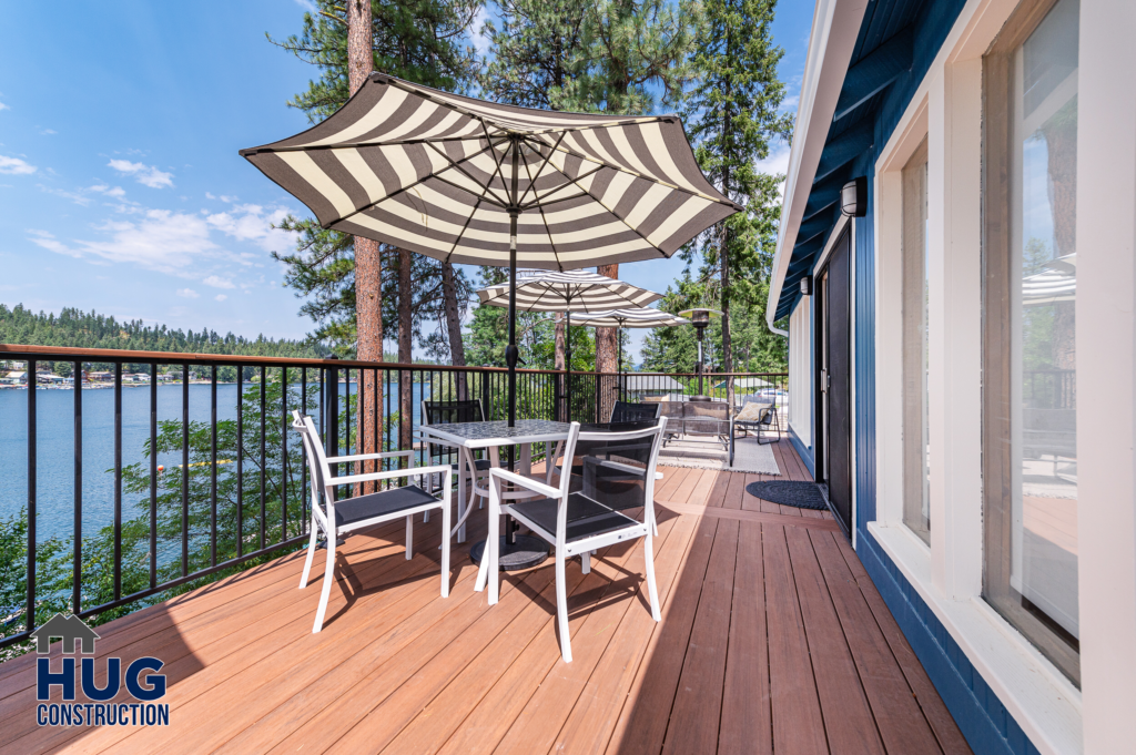 A wooden deck with outdoor furniture and an umbrella overlooking a lake with trees in the background at Silver Beach Cabin.