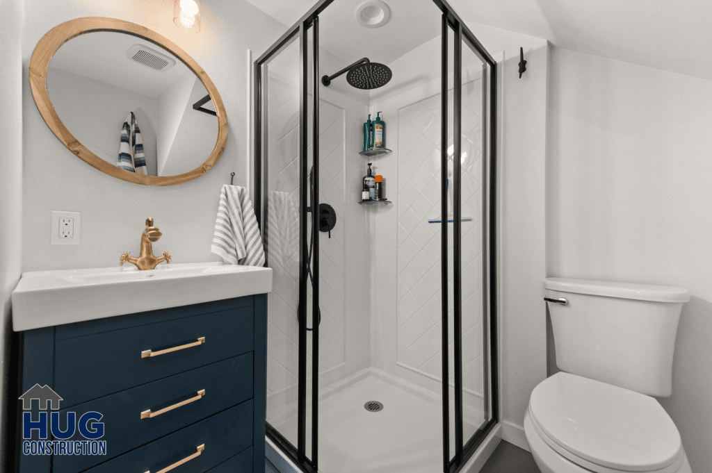 Modern "Silver Beach Cabin" bathroom interior with a navy blue vanity, round mirror, glass-enclosed shower, and white walls.