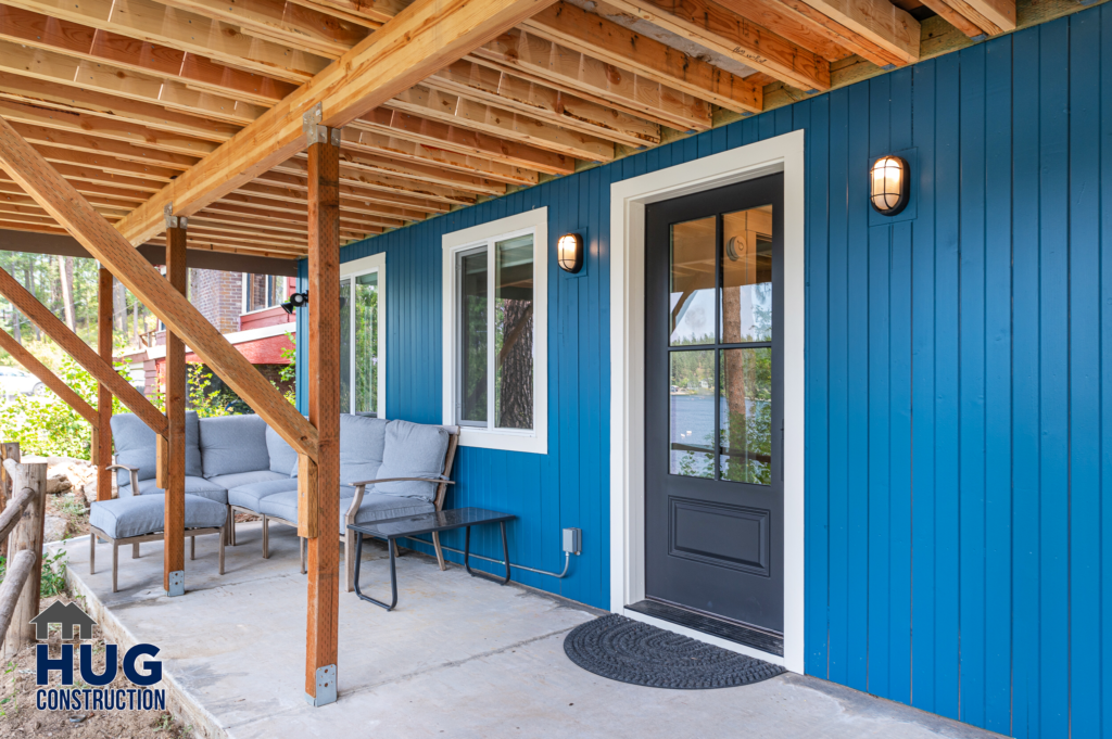 A newly constructed Silver Beach cabin's blue siding with a covered porch, featuring a black front door and outdoor seating.