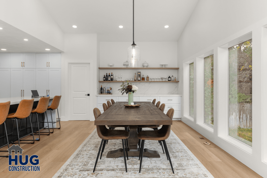 Modern dining room within a 2-story addition and kitchen remodel, featuring a wooden table, leather chairs, white cabinetry, and pendant lighting, complemented by large windows with a view of trees outside