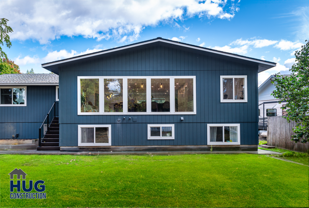 A modern blue 2-story house with large windows, a kitchen remodel, and a well-maintained lawn, featuring the logo "hug construction" in the corner.