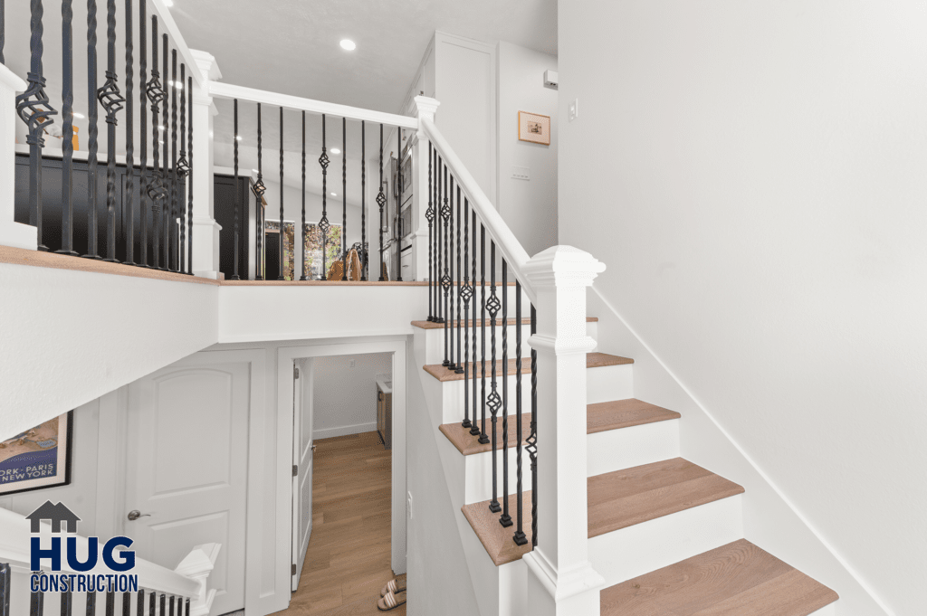 A modern stairway with white walls, wooden steps, and decorative metal balusters, leading to the upper level of a house or building, including a 2-story addition and kitchen remodel.